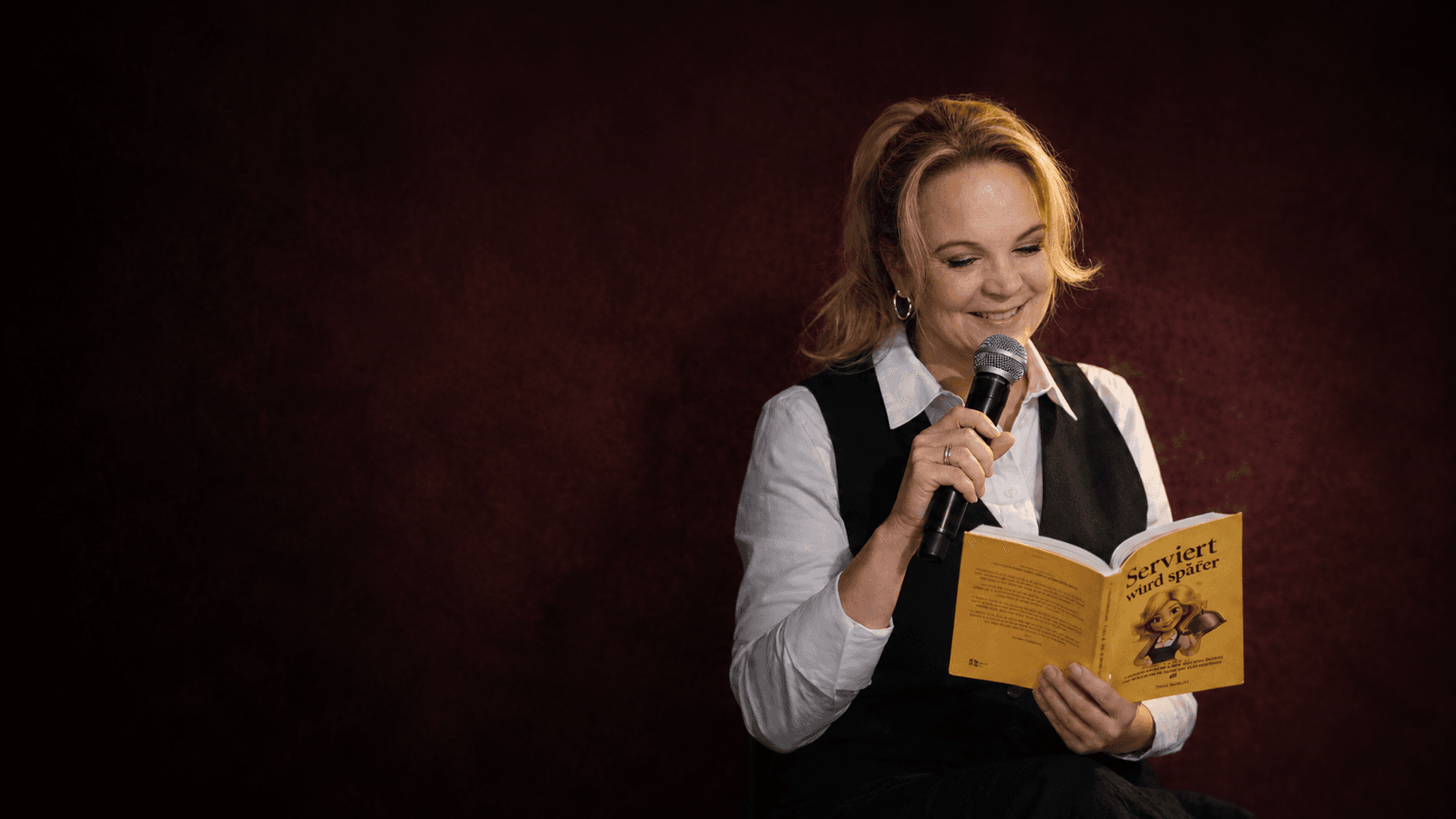 Jana Rensle liest mit Mikrofon aus ihrem Buch „Serviert wird später“